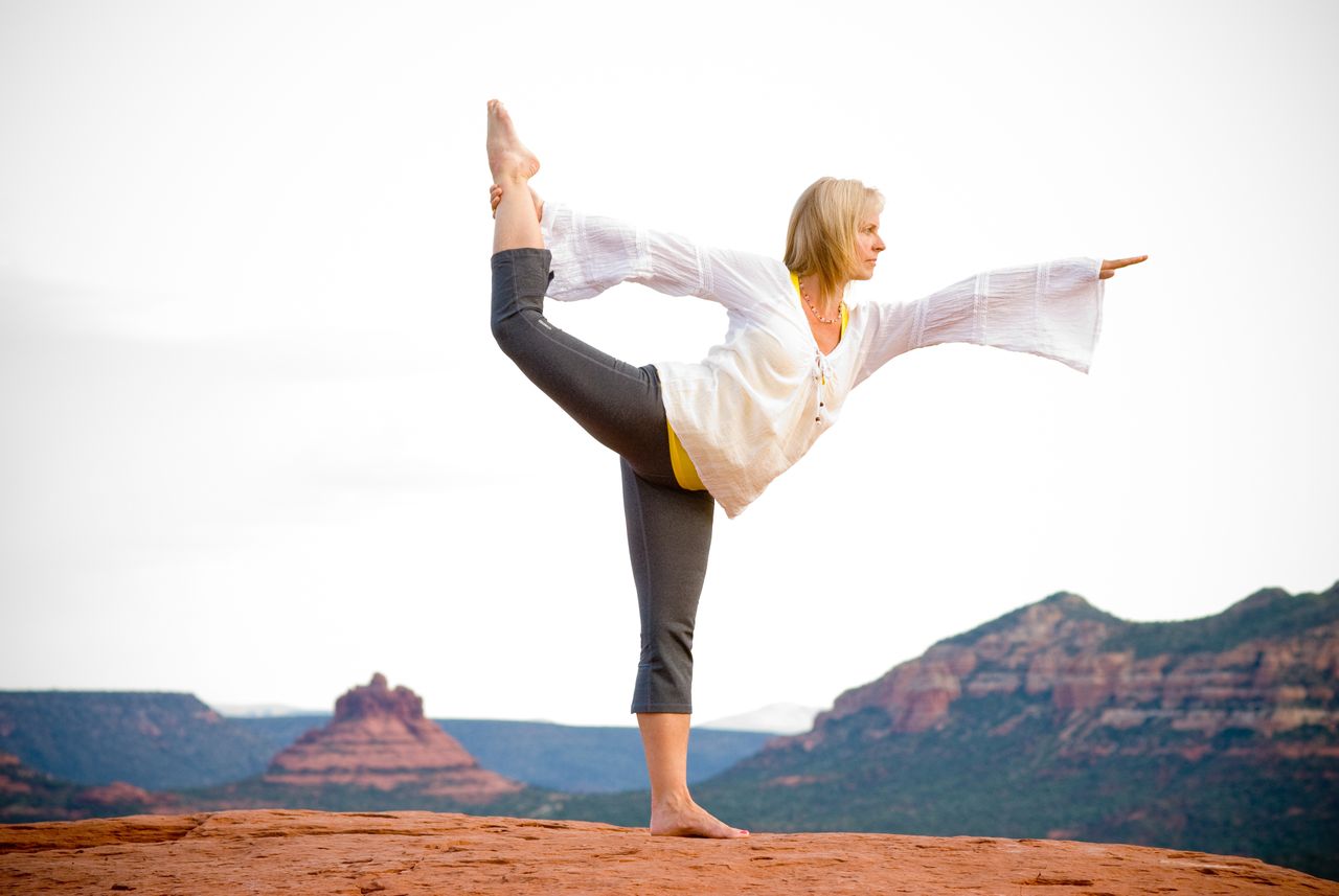 our-services-01 A woman practicing yoga in nature on a rocky mountain landscape during daylight.